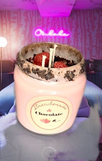 a pink candle with strawberries in it on a bed